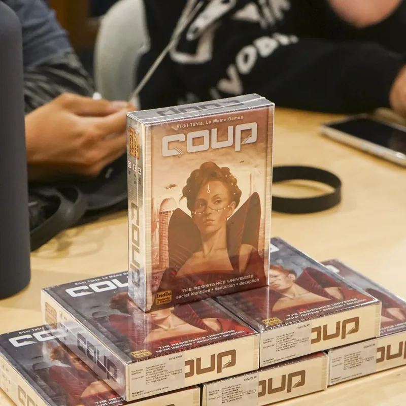 Fresh Coup stock stacked on a reseller demo table with players around it