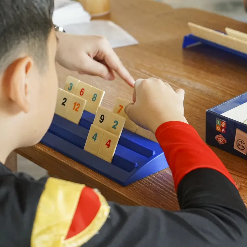 Kids mid-game around a Rummikub set on a wooden table