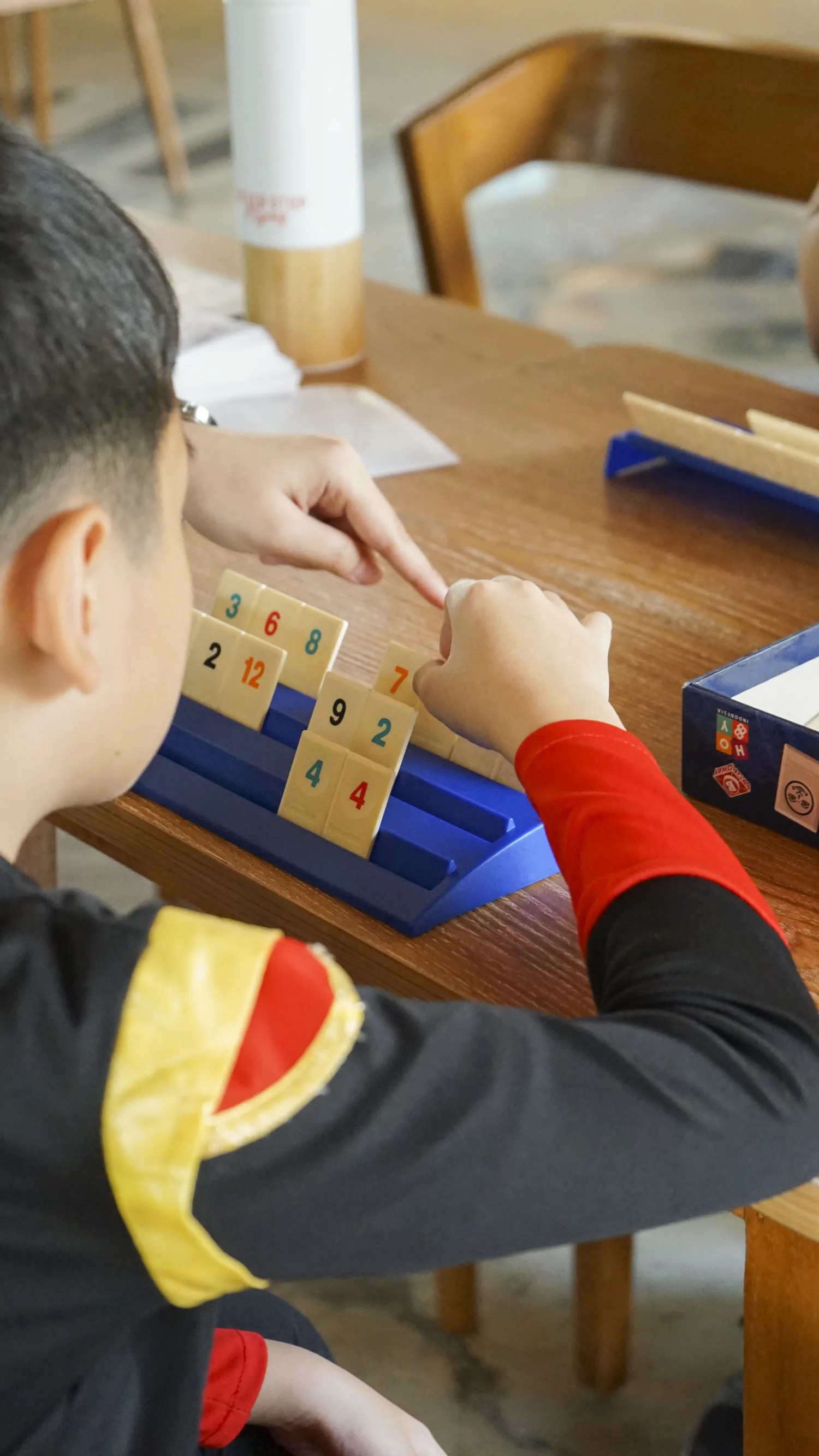 Kids mid-game around a Rummikub set on a wooden table